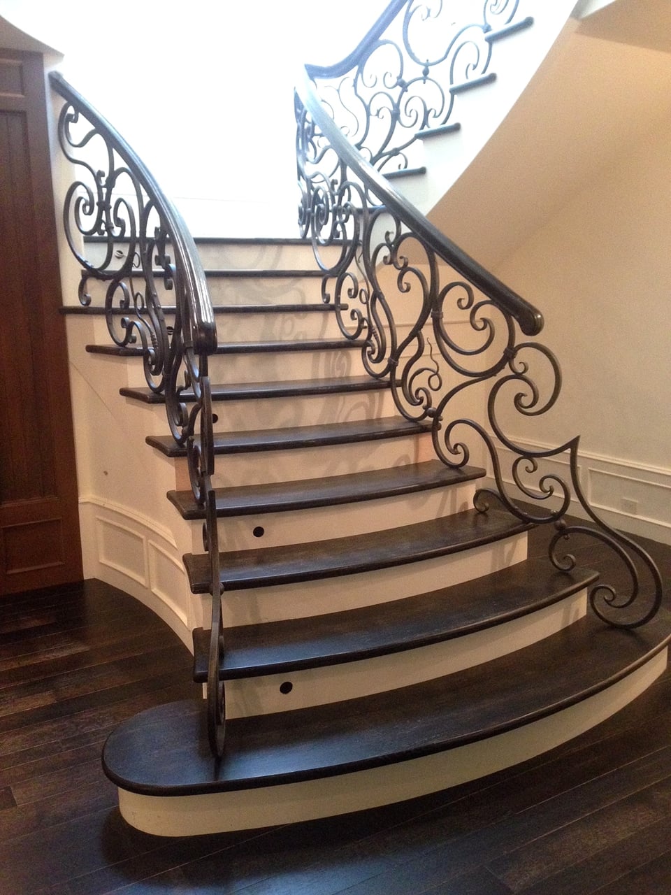 Curved hardwood staircase with ornate wrought-iron railing